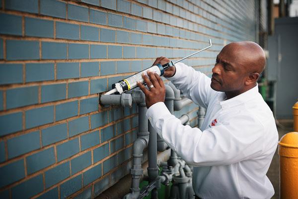 An Orkin Pro putting caulk around a pipe-600x400